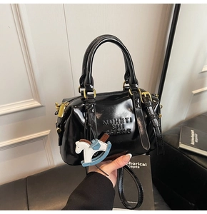 Detail of black patent leather boston bag with embossed letters and a rocking horse charm