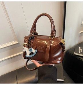 Detail of dark brown glossy Boston bag with embossed lettering and horse charm