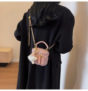 Pink tweed crossbody box bag with gold chain and plush ball charm on wool coat