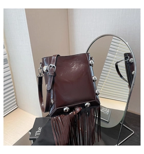 Detail view of dark brown glossy leather bucket bag with silver studs and long fringe