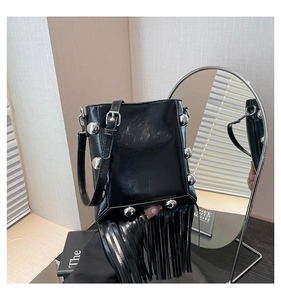 Detail of black patent leather bucket bag featuring silver rivets and long fringe tassels