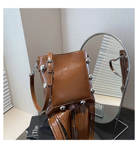 Detail view of brown glossy tassel bucket bag with large silver spherical rivets