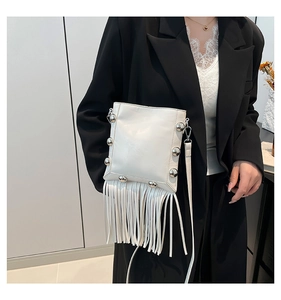 Detail of white leather crossbody bag featuring silver rivets and long fringe tassels