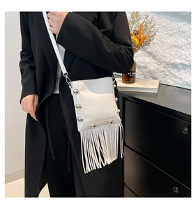 Close-up of white fringe crossbody bucket bag with silver studs on a black coat