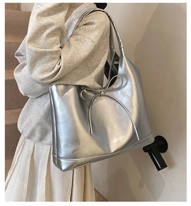 Detail of metallic silver tote bag with decorative bow and glossy oil wax leather finish