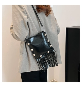 Detailed view of black patent leather crossbody bag with silver studs and long fringe