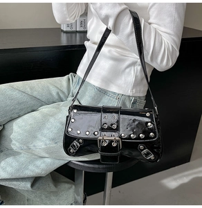 Detail of punk style black patent leather shoulder bag with silver studs and metal buckle