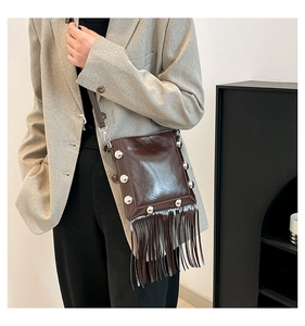 Detail of dark brown patent leather bucket bag with silver rivets and long fringe tassels