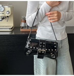 Detail of black patent leather underarm bag with silver rivets and biker-style buckles
