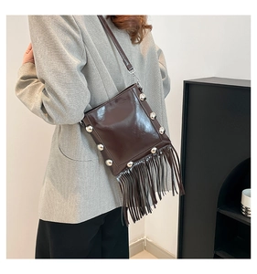 Detail of dark brown glossy bucket bag featuring silver rivets and long leather tassels