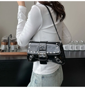 Close-up of black patent leather underarm bag with silver rivets and metallic buckle