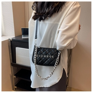Detail of black quilted crossbody bag with silver chunky chain and metal letter charm