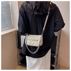Detailed shot of beige quilted crossbody bag with silver chain and metal brand logo