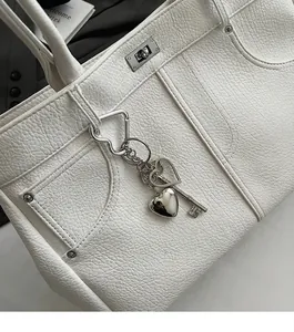 Nahaufnahme des silbernen Herz- und Schlüsselanhängers an einer weißen Ledertasche