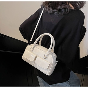 Detail of a creamy white glossy oil wax leather Boston bag featuring two front flap pockets