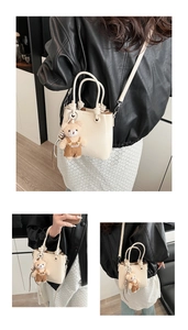 Detail of off-white leather tote bag with lychee texture and plush bear charm