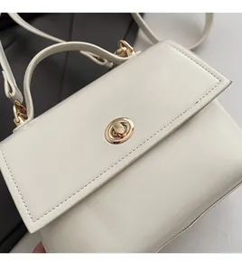Detail shot of white small square bag showing soft leather texture and golden oval twist lock