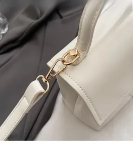 Detailed close-up of golden metal hardware and leather strap on white square crossbody bag
