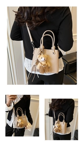 Detail of beige lychee textured bucket bag with cute brown plush bear charm and knotted handles