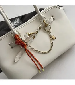 Detail of cream tote bag featuring orange rope strap, gold chain, and heart pendant