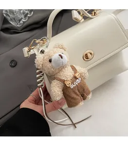 Detail of a beige teddy bear bag charm with corduroy overalls and golden metal clasp