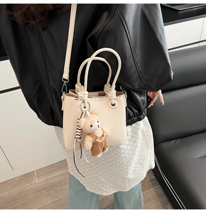 Detail of cream pebbled leather bucket bag featuring a cute plush bear pendant