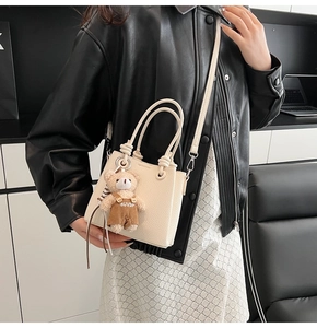 Detail of cream white textured mini bucket bag featuring a cute bear plush keychain charm