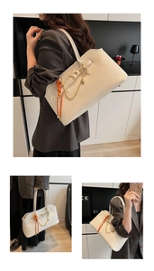 Detail view of large cream tote bag with orange woven charm and gold heart pendant chain