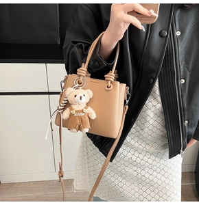 Detail of camel tote bag with litchi grain texture and a cute plush bear charm