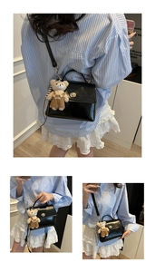 Detail view of black patent leather crossbody bag with teddy bear charm and metal buckle