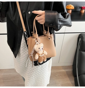 Detail of khaki pebbled leather bucket bag featuring a cute teddy bear charm pendant