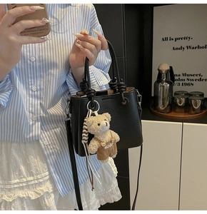 Detail of black lychee leather crossbody bag with knot handle and cute bear charm pendant