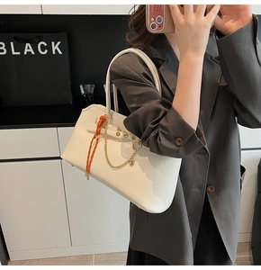 Detail of white leather-textured shell tote bag with gold chain and orange woven strap
