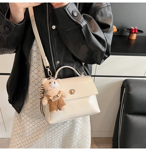 Detail of cream glossy handbag with golden turn-lock and cute plush bear accessory