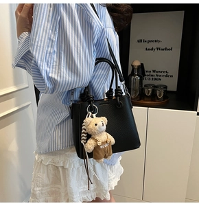 Detail of black lychee grain bucket bag featuring a knotted handle and plush bear charm