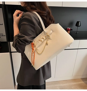 Detail of cream tote bag with gold heart charm and orange printed handle scarf