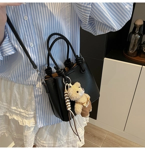 Detail of black lychee texture bucket bag with adjustable strap and cute bear charm