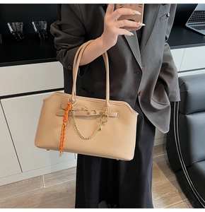 Detailed view of apricot leather tote bag featuring gold chain and orange woven charm