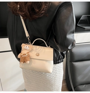 Detail of off-white crossbody bag with metal twist lock and cute teddy bear charm