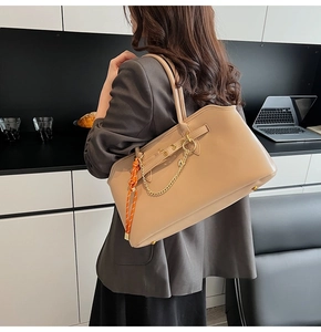 Detail of beige tote bag featuring gold chain and patterned scarf on a grey suit model