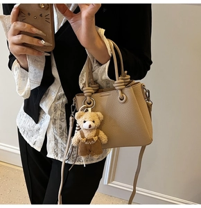 Detail of beige lychee grain crossbody bag with knotted handle and cute bear pendant