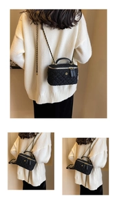 Detail of black tweed crossbody box bag with gold floral buckle and woven chain strap