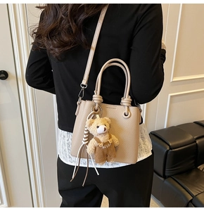 Detail of beige pebble leather bucket bag with a cute bear charm and removable strap