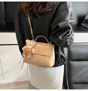 Close-up of stylish cream crossbody bag with golden clasp and cute bear charm pendant