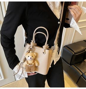 Detail of beige lychee texture bucket bag with cute bear pendant and leather handle