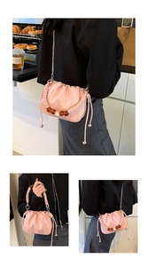 Close-up of pink ruched bucket bag with woven handle, large pearls, and metal chain strap