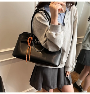 Black leather tote bag detail with orange woven knot and silver chain shown on model
