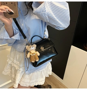 Close-up of a black glossy crossbody bag with bear charm and metallic lock detail