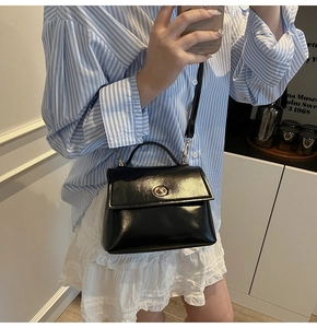 Classic black glossy leather crossbody bag featuring a golden circular metal clasp detail