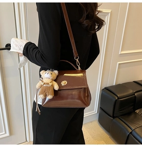 Detail of dark brown glossy leather crossbody bag with teddy bear charm shown on model